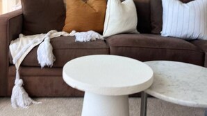 A living room with a brown sofa, white and brown cushions, a white round coffee table, and a framed picture of birds on water.