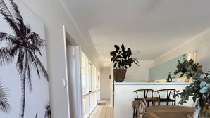 A hallway leading to a dining area with a wooden table and chairs, a large potted plant, and a wall with a palm tree mural.