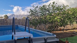 An outdoor swimming pool with a wooden fence and a tree in the background. - Vacation apartment with panoramic views at Finca Gran Calma - ideal for hikers (Santa Lucía de Tirajana)