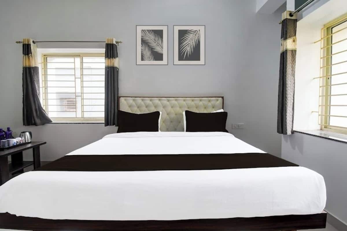 A hotel room with a large bed, two framed leaf artworks on the wall, and a window with curtains.