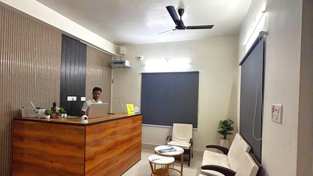A modern reception area with a wooden desk, a seating area with a sofa and two chairs, a ceiling fan, and a large screen on the wall. - Hotel Crystal INN (Bhubaneshwar)