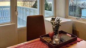 Ein Essbereich mit Tisch für zwei Personen, einem Stuhl, einer Blumenvase und einem Tablett mit Kerze und Buch.