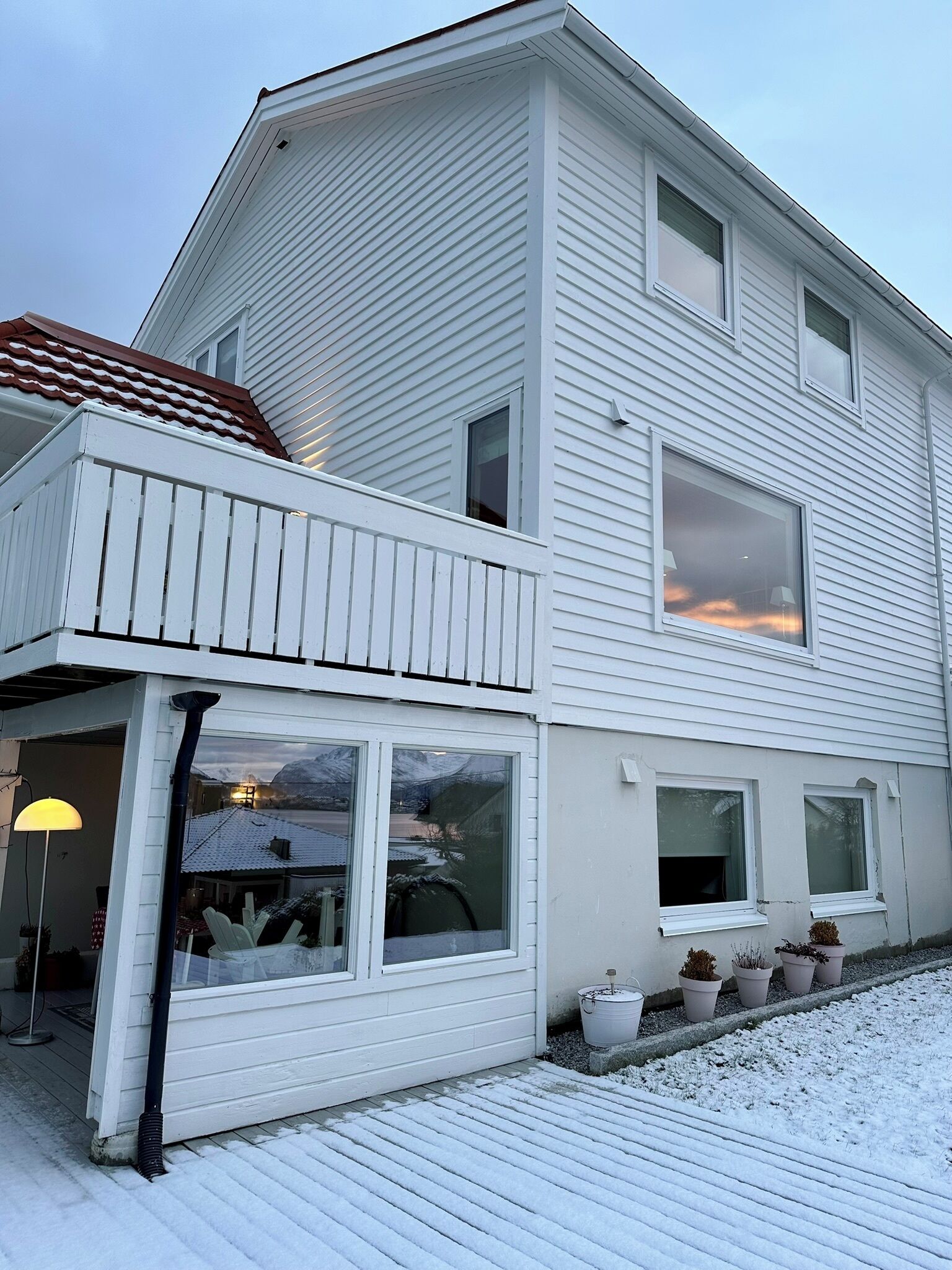 Ett tvåvåningshus med en balkong, stora fönster och krukväxter.