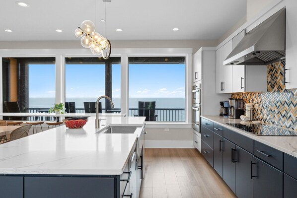A modern kitchen with a large island, a view to the sea, and a herringbone-patterned backsplash.