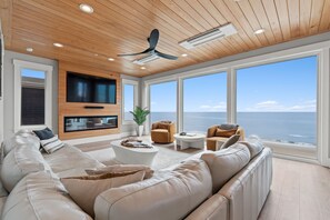 A spacious living room with a large sectional sofa, a flat-screen TV, a ceiling fan, and a view of the ocean.