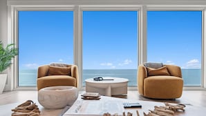 Sala moderna com uma janela ampla com vista para o mar, dois poltronas, uma mesa de centro e um recipiente com canela em pau.