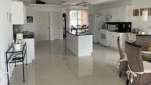 A modern kitchen with white cabinetry, a central island, and a dining area with wicker chairs.