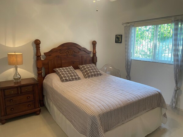 A bedroom with a wooden bed frame, a bedside table with a lamp, and a window with curtains.