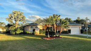 A single-story house with a garage, surrounded by a well-maintained lawn and palm trees.