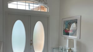 A modern entryway with a double door, a glass console table, a hanging light fixture, and a framed artwork on the wall.
