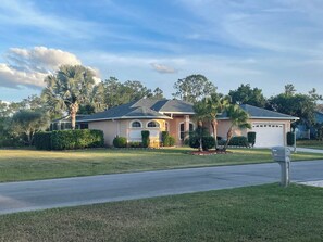 A single-story house with a garage, surrounded by a well-maintained lawn and palm trees. - The ArtHouse - modern, stylishly furnished vacation home with pool! (Lehigh Acres)
