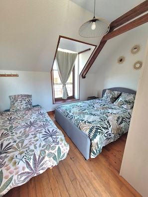 A bedroom with two beds, a window with curtains, a hanging light fixture, and a mirror on the wall.