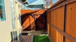 Un espacio exterior estrecho con un camino de ladrillo, césped artificial verde y una valla de madera.
