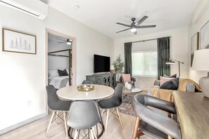 A modern living room with a round dining table, black chairs, a sofa, a TV, and a ceiling fan.
