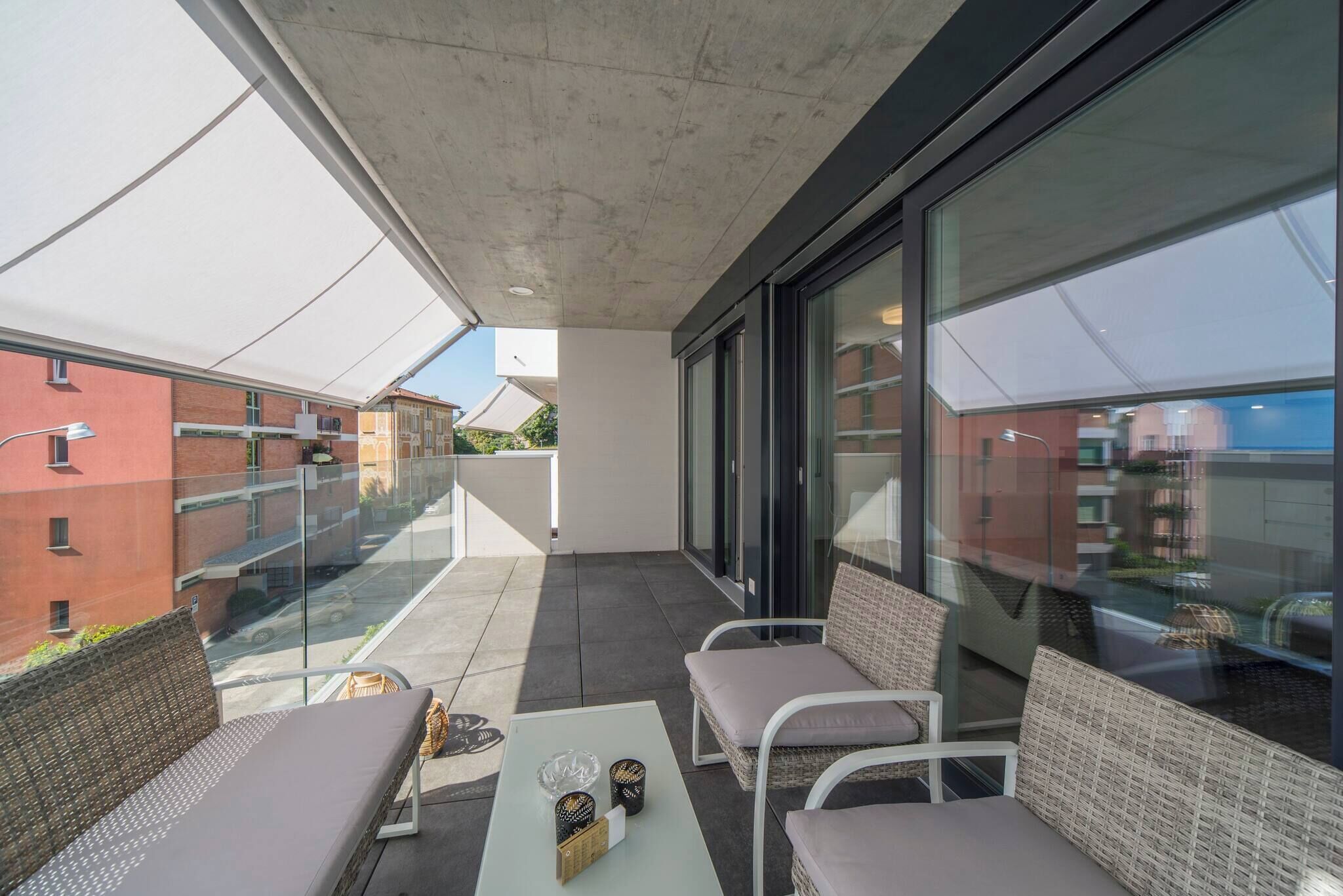 A modern balcony with wicker furniture, a glass railing, and a view of the cityscape.
