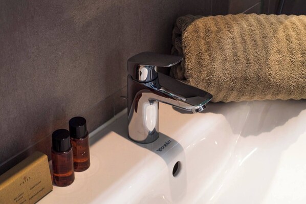 A bathroom sink with a chrome faucet, two small bottles, and a towel on the side.