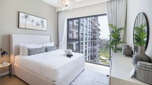 Een moderne slaapkamer met een groot bed, een nachtkastje, een spiegel en een groot raam met uitzicht op een gebouw.