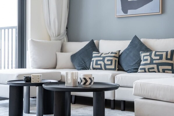 A modern living room with a white sofa, two black coffee tables, and decorative pillows. - StayShort - Chic 1-Bed for 4 in Prime Dubai Hills Location! (Dubai Hills)