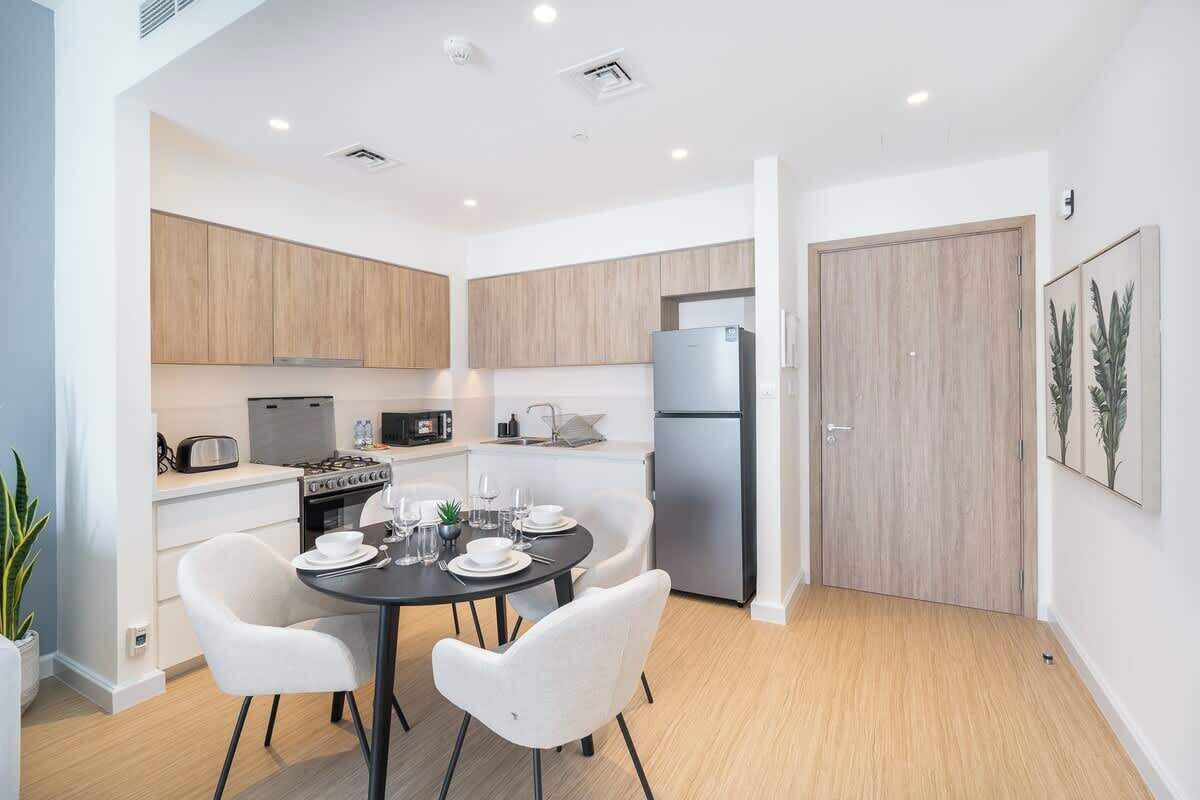 A modern kitchen with wooden cabinets, a dining table with white chairs, a refrigerator, and a stove.