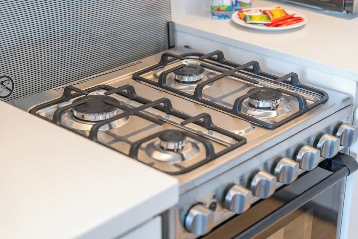 Una cucina con piano cottura a gas, forno e un bancone bianco.