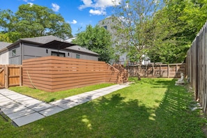 A backyard with a wooden fence, a paved walkway, and a grassy lawn.