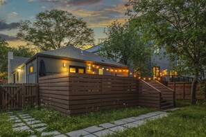 A house with a wooden fence, a staircase leading to a deck, and string lights.
