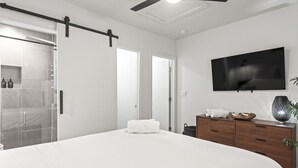 A modern bedroom with a large bed, a TV mounted on the wall, and a sliding door leading to a shower area. - Hot Tub | Fully-Fenced Yard |The Bubbly Suite (Atlanta)