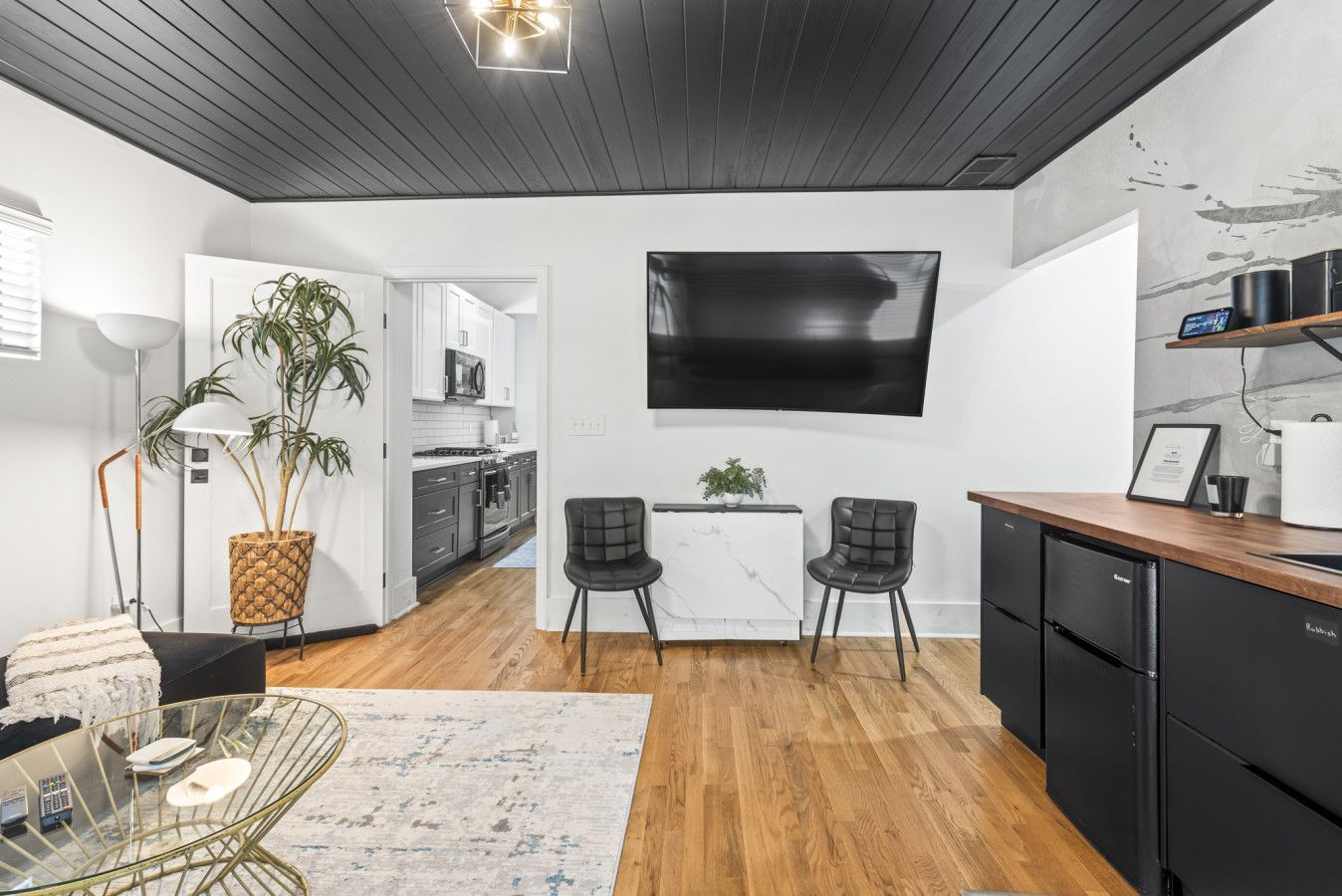 A modern kitchen with a flat-screen TV, two chairs, a dining table, and a coffee machine.