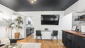 A modern kitchen with a flat-screen TV, two chairs, a dining table, and a coffee machine. - Hot Tub | Fully-Fenced Yard |The Bubbly Suite (Atlanta)