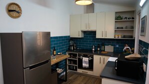 Een moderne keuken met een roestvrijstalen koelkast, een inbouwoven en een magnetron. Er is een spoelbak met een kraan, een aanrecht met diverse keukenbenodigdheden, en een raam boven de spoelbak.