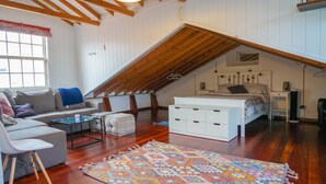 Slaapkamer in loftstijl met schuine plafonds, een bed, nachtkastje, kapstok, bank, salontafel en een kamerbreed tapijt met dessin.