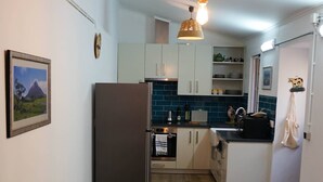 Een kleine keuken met witte kastjes, een houten eettafel met vier stoelen en een hangende lamp.