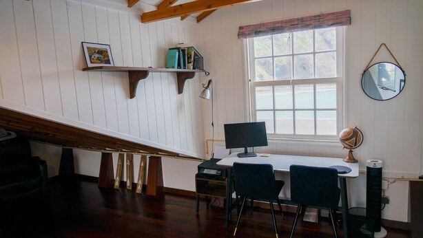 Een kamer met een bureau, twee stoelen, een computer, een wereldbol en een raam met uitzicht op zee.