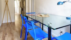 Un espace repas moderne avec une table en verre, des chaises bleues et une suspension jaune.