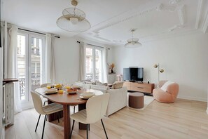 A spacious living room with a dining area, a sofa, a TV, and a balcony.