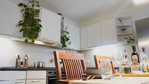 Eine Küche mit weißen Schränken, einem Holzhocker, einem Esstisch mit einem Glas und verschiedenen Flaschen.