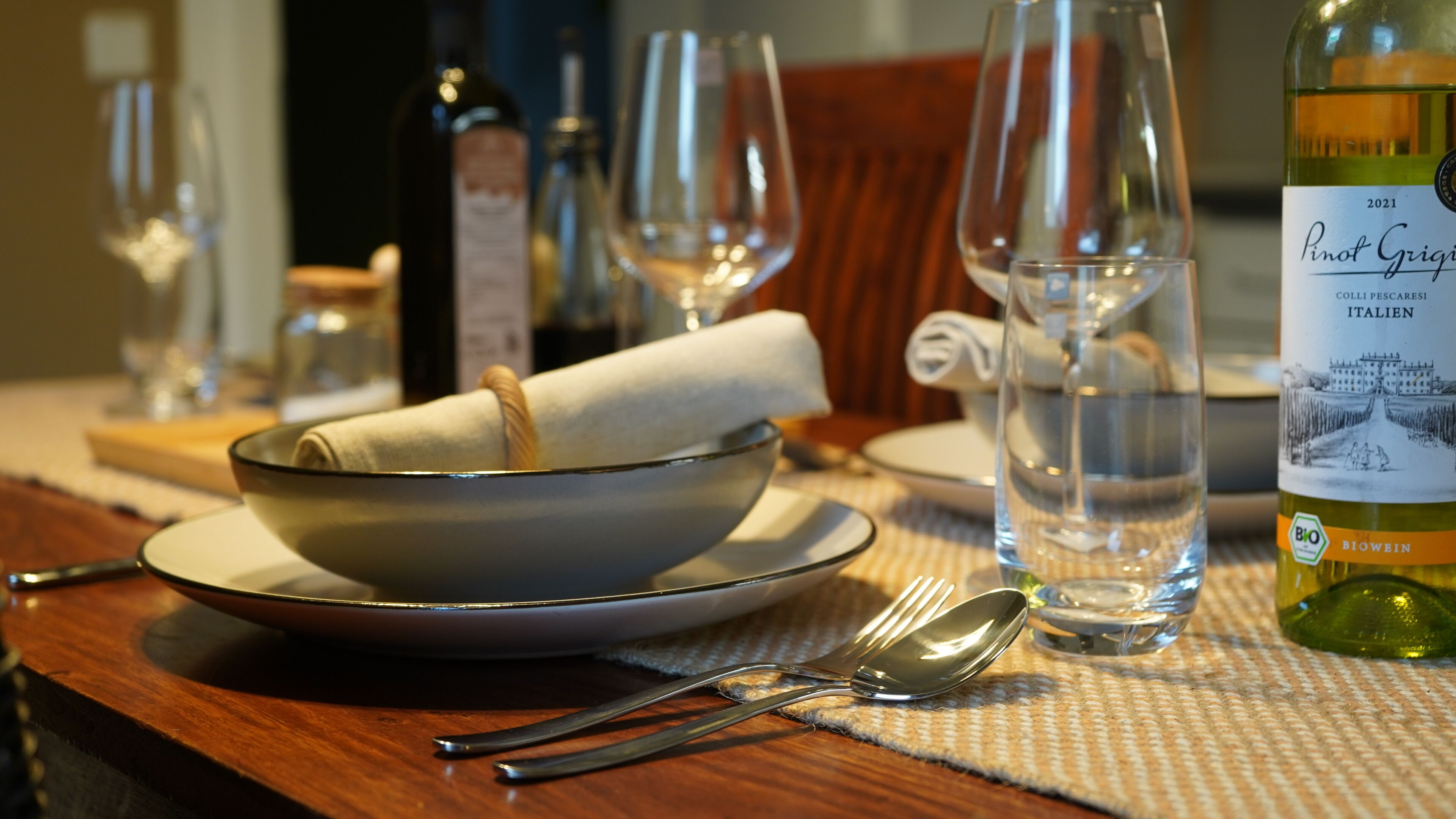 A dining table with a bowl, plates, cutlery, and a wine bottle.