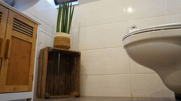 Een badkamer met toilet, houten kastjes en een klein houten krukje met een plantje.
