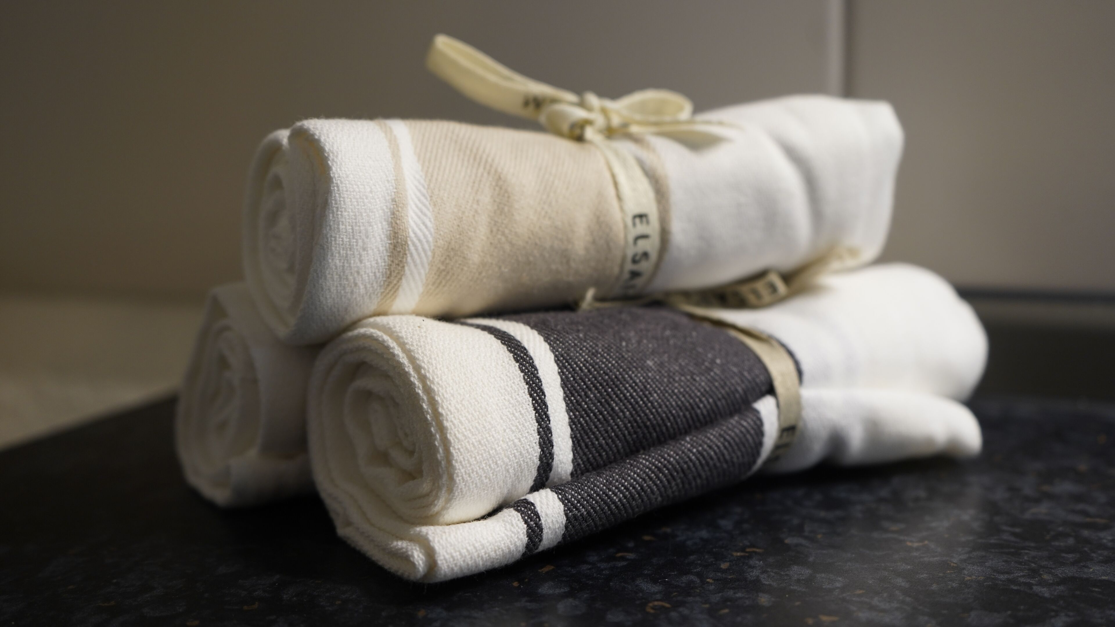 Three rolled towels with a black and white stripe, tied with a ribbon, on a dark surface.