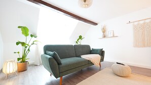 Ein modernes Wohnzimmer mit einem grünen Sofa, Holzboden und einem großen Fenster, das natürliches Licht hereinlässt.