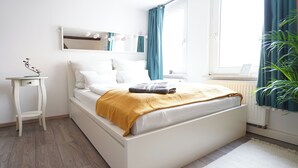Ein Schlafzimmer mit Bett, Nachttisch, Spiegel, einem Fenster mit Vorhängen und einer Heizung.
