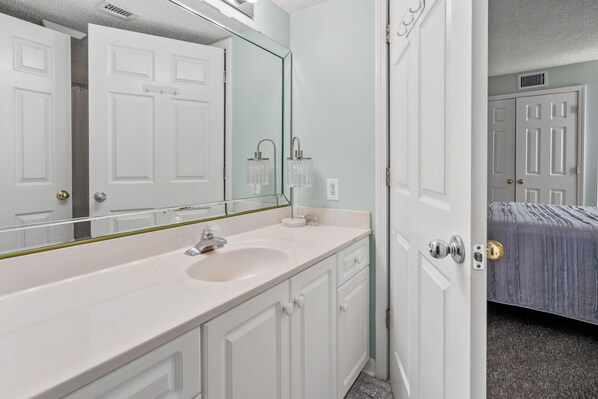 A bathroom with a white sink, mirror, and cabinets. - Ashworth 1801 4 Bedroom Condo (North Myrtle Beach)