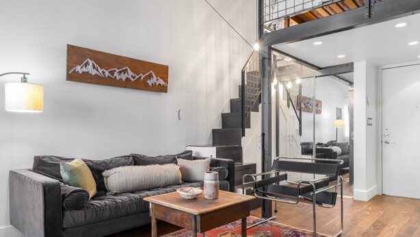 A modern living room with a sofa, a coffee table, a rug, and a staircase leading to an upper level. - Tomboy Lodge 144 1 Bedroom Condo (Telluride)