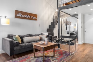 A modern living room with a sofa, a coffee table, a rug, and a staircase leading to an upper level.