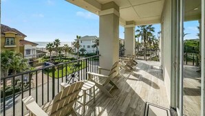 Un balcón con vista al océano, palmeras y casas vecinas.