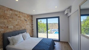 Ein modernes Schlafzimmer mit Steinwand, großem Bett und Blick auf Pool und Grünflächen.