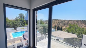 Ein modernes Interieur mit großen Glasüren, die auf einen Balkon mit Blick auf einen Pool und eine hügelige Landschaft führen.
