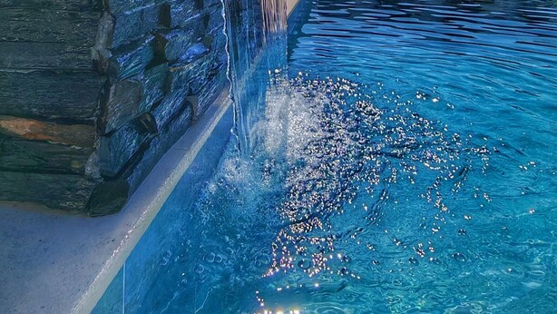 Ein Pool mit Wasserfall, klarem blauen Wasser und einer Steinwand.