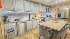 Eine moderne Küche mit weißen Schränken, einem Edelstahl-Geschirrspüler, einem Holztisch mit grauen Stühlen und einem eingebauten Backofen.