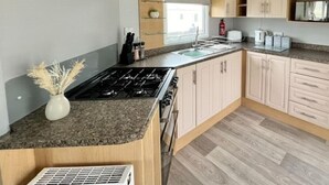 Moderni keittiö, jossa on kaasuliesi, pesuallas ja puukehikoiset kaapit.